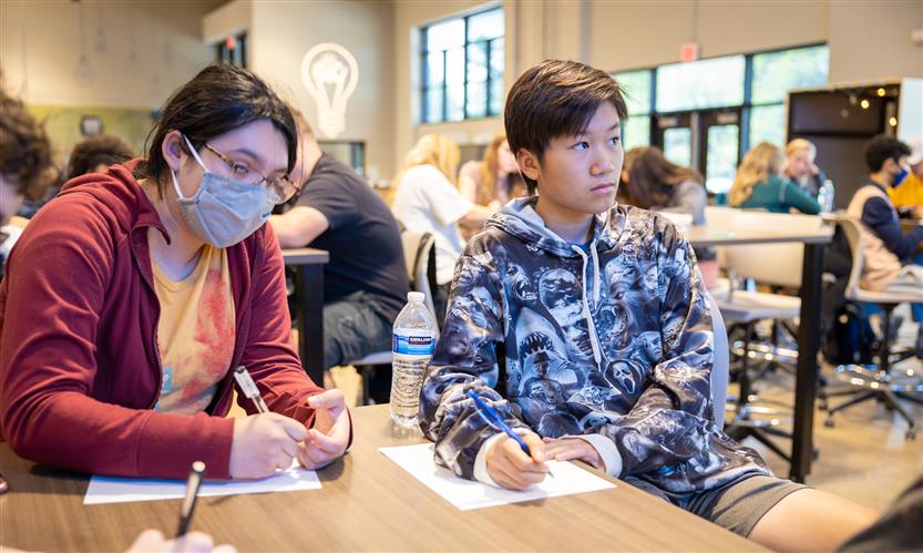 Students listen to a presenter while sitting at a table